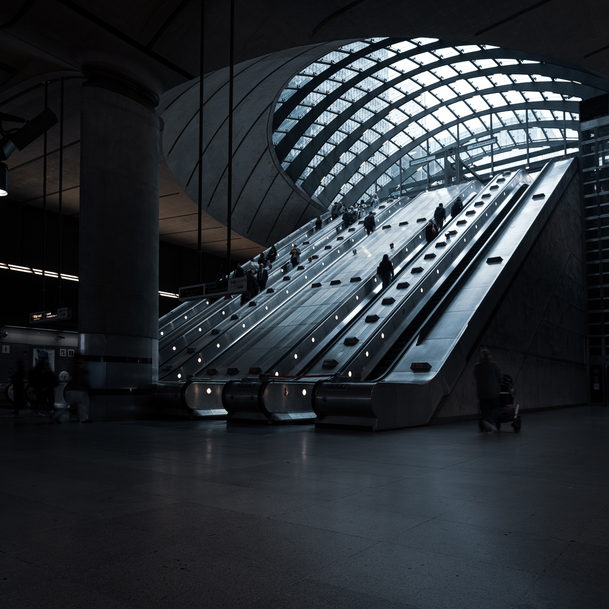 Escalators inside Canary Wharf Station, underneath curved glass canopy.