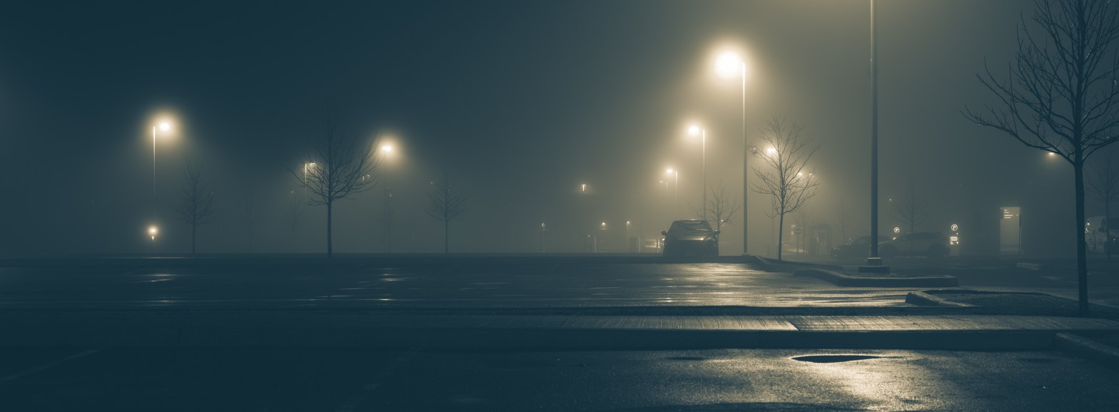 Foggy night in the staff parking lot at Providence Care Hospital in Kingston, Ontario, with streetlights glowing through mist and a single parked car.