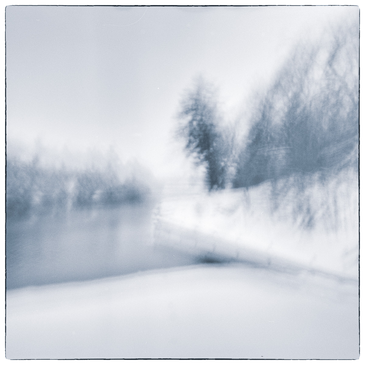 Blurred winter canal landscape created through intentional camera movement, with soft trees and shoreline dissolving into abstraction.