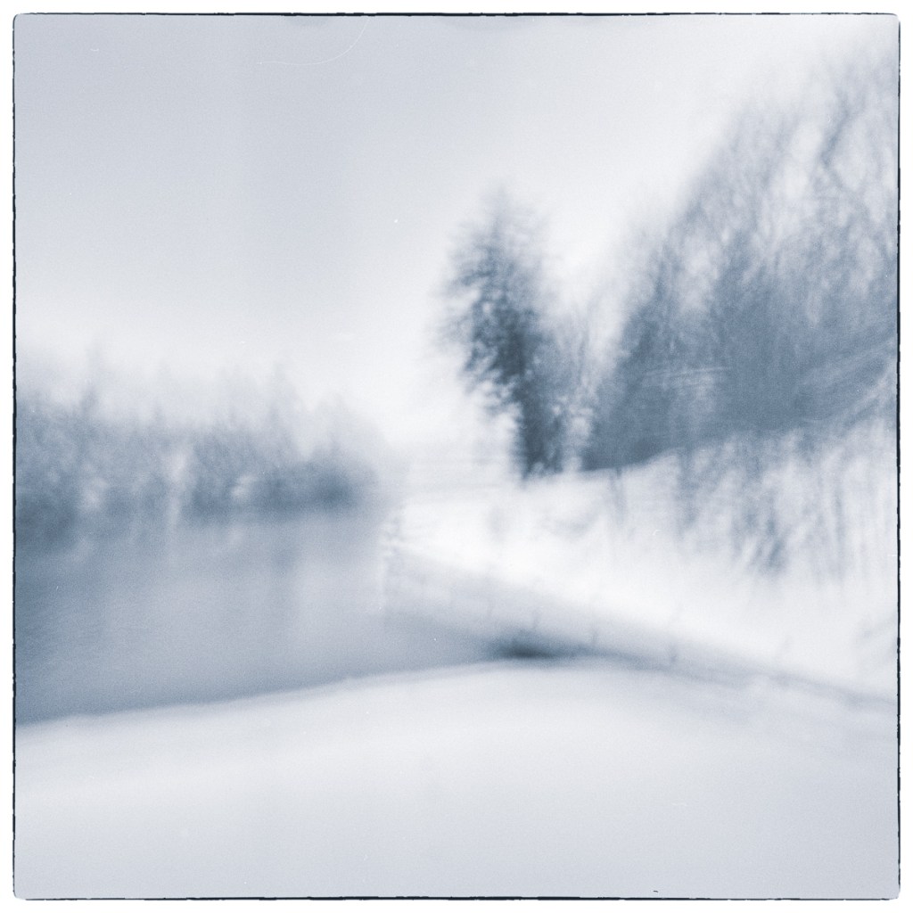 Blurred winter canal landscape created through intentional camera movement, with soft trees and shoreline dissolving into abstraction.