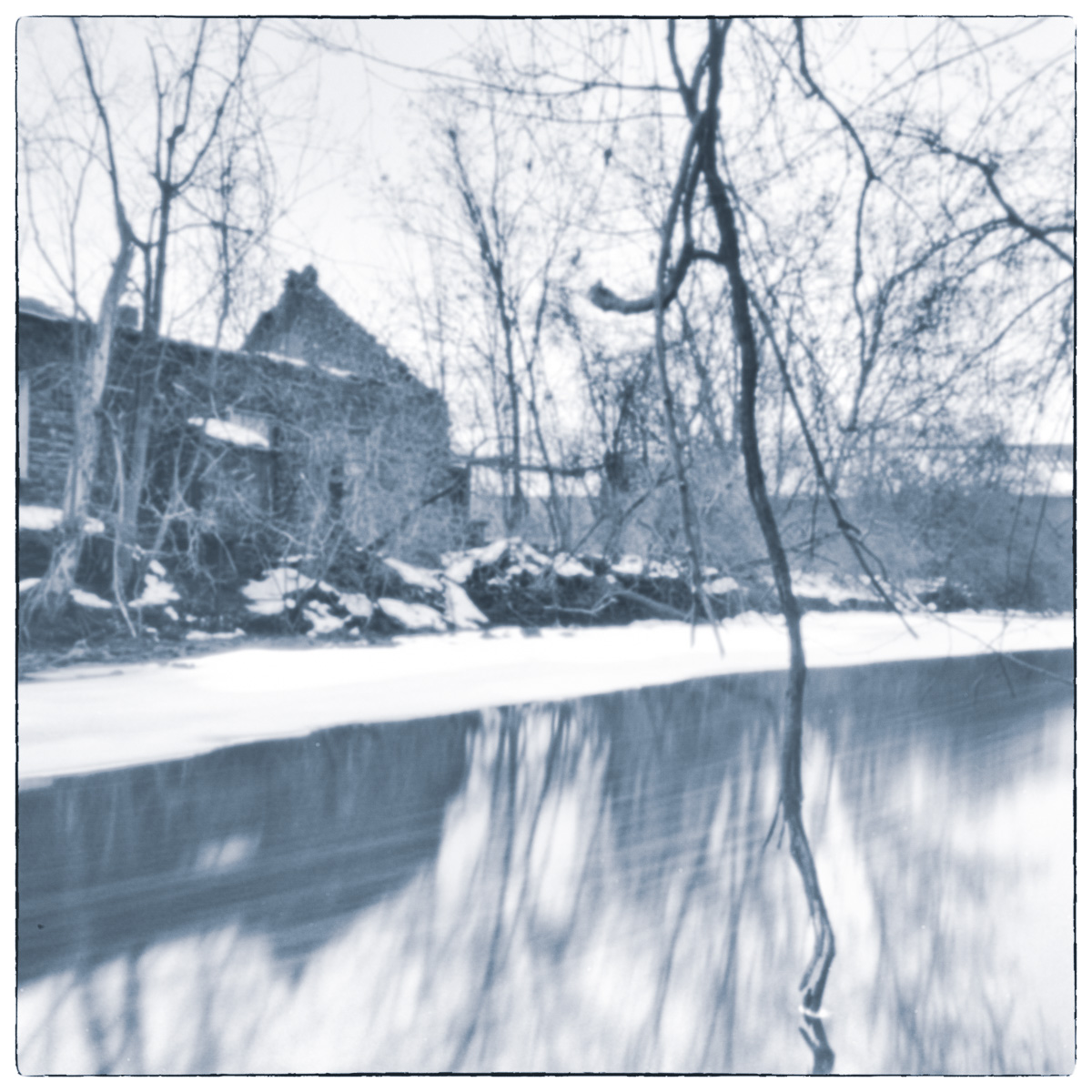 Blurred winter canal scene with bare trees and historic stone building reflected in water.