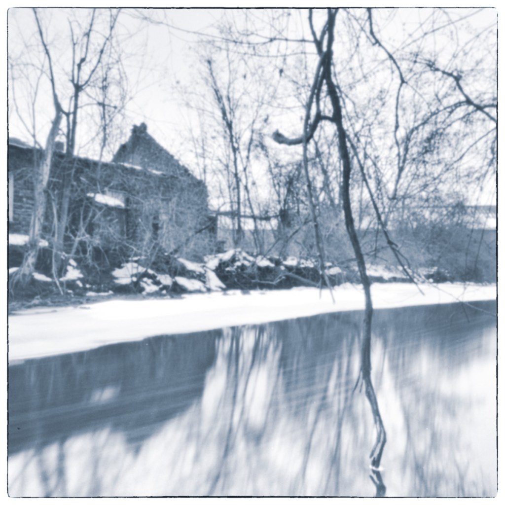 Blurred winter canal scene with bare trees and historic stone building reflected in water.