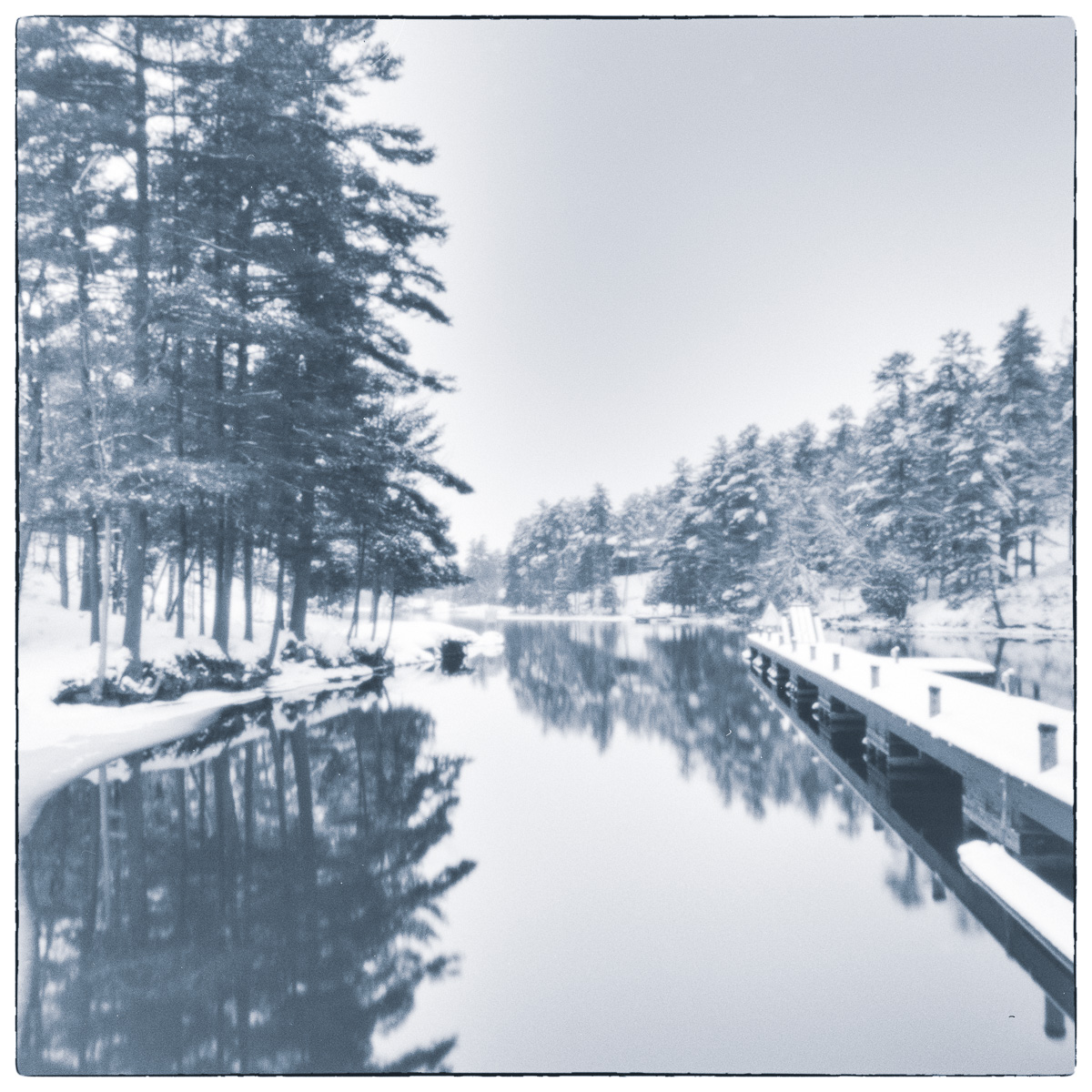 Winter canal scene with snow-covered lock walls and trees reflected in calm water.