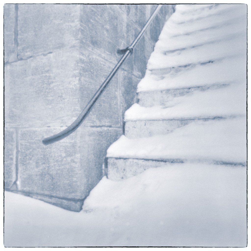 Long-exposure black and white photograph of snow-covered concrete steps and a metal handrail at Old Slys Lock in Smiths Falls, Ontario.
