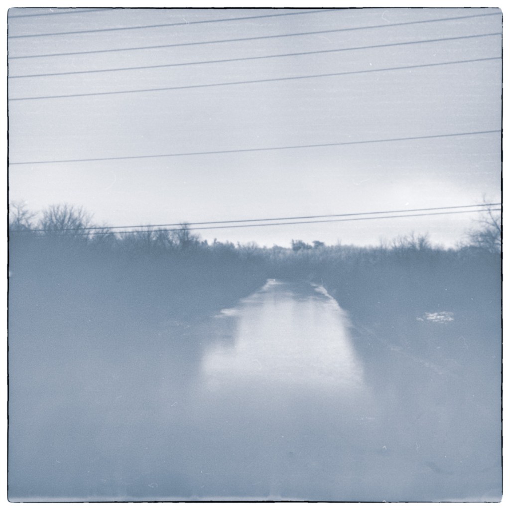 Long-exposure black and white pinhole photograph of the Rideau Canal near Newboro Lock, viewed from the Highway 42 bridge beneath overhead utility lines.