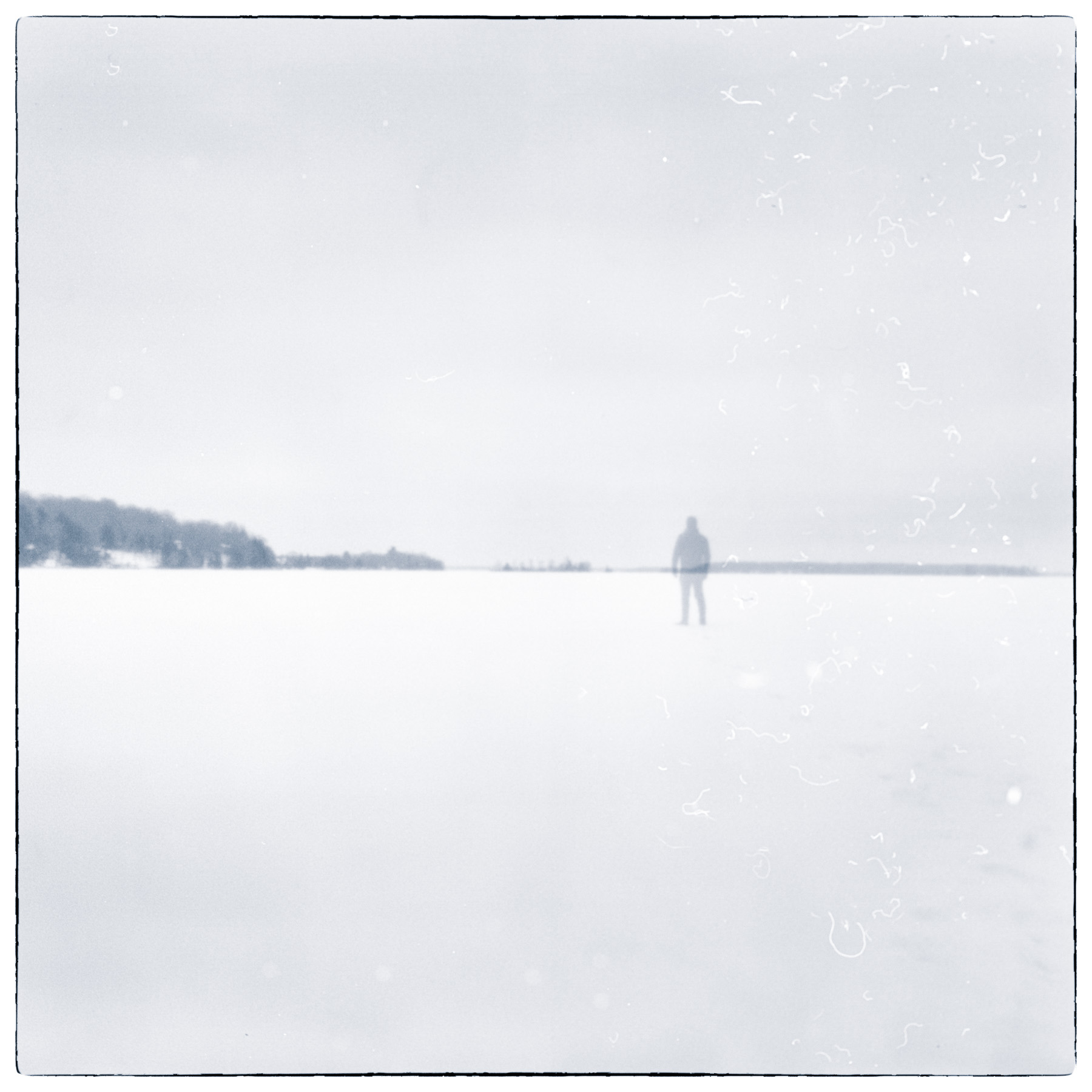 Solitary figure standing on a frozen landscape in winter, photographed in soft monochrome tones.