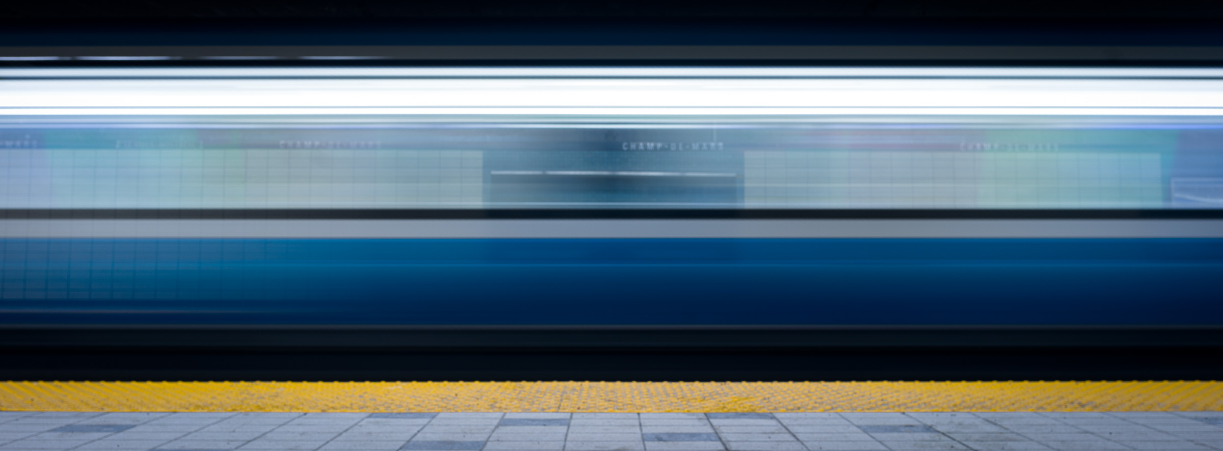 Long-exposure colour photograph of a train blurring across the platform at Champ-de-Mars station in the Montréal Métro.