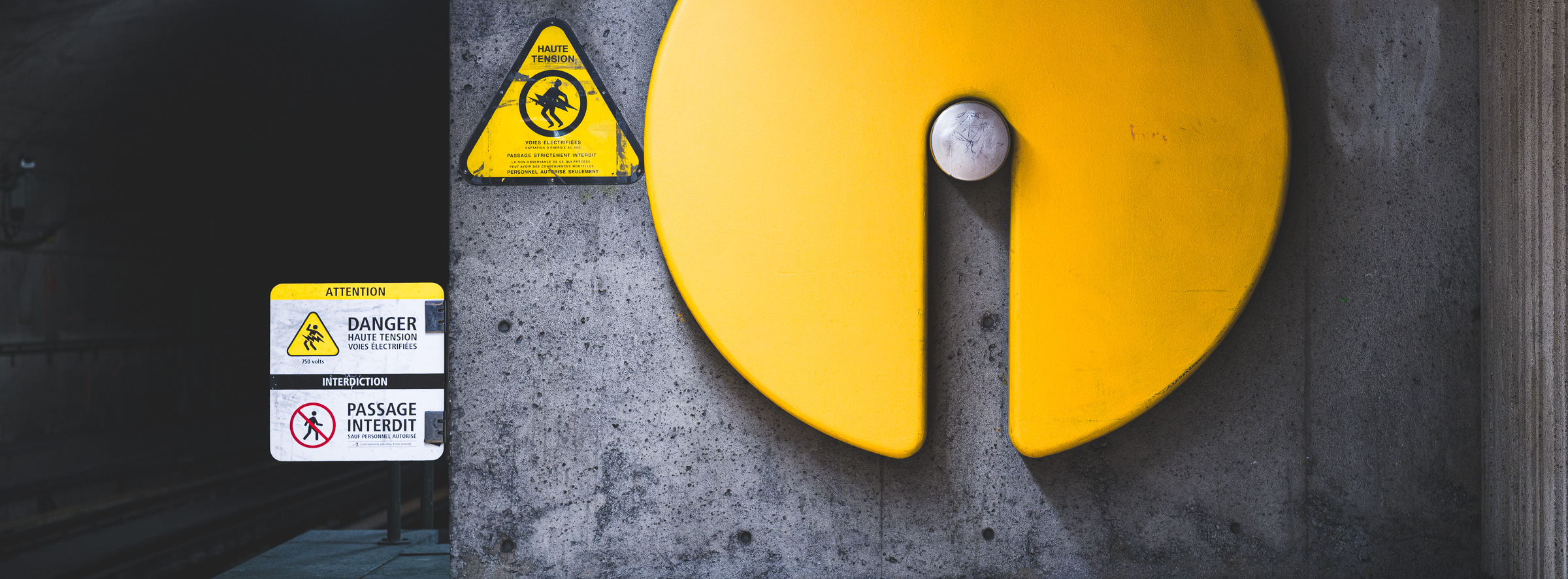 Panoramic colour photograph of warning signs and a large yellow circular wall element at the end of the Villa-Maria platform in the Montréal Métro.
