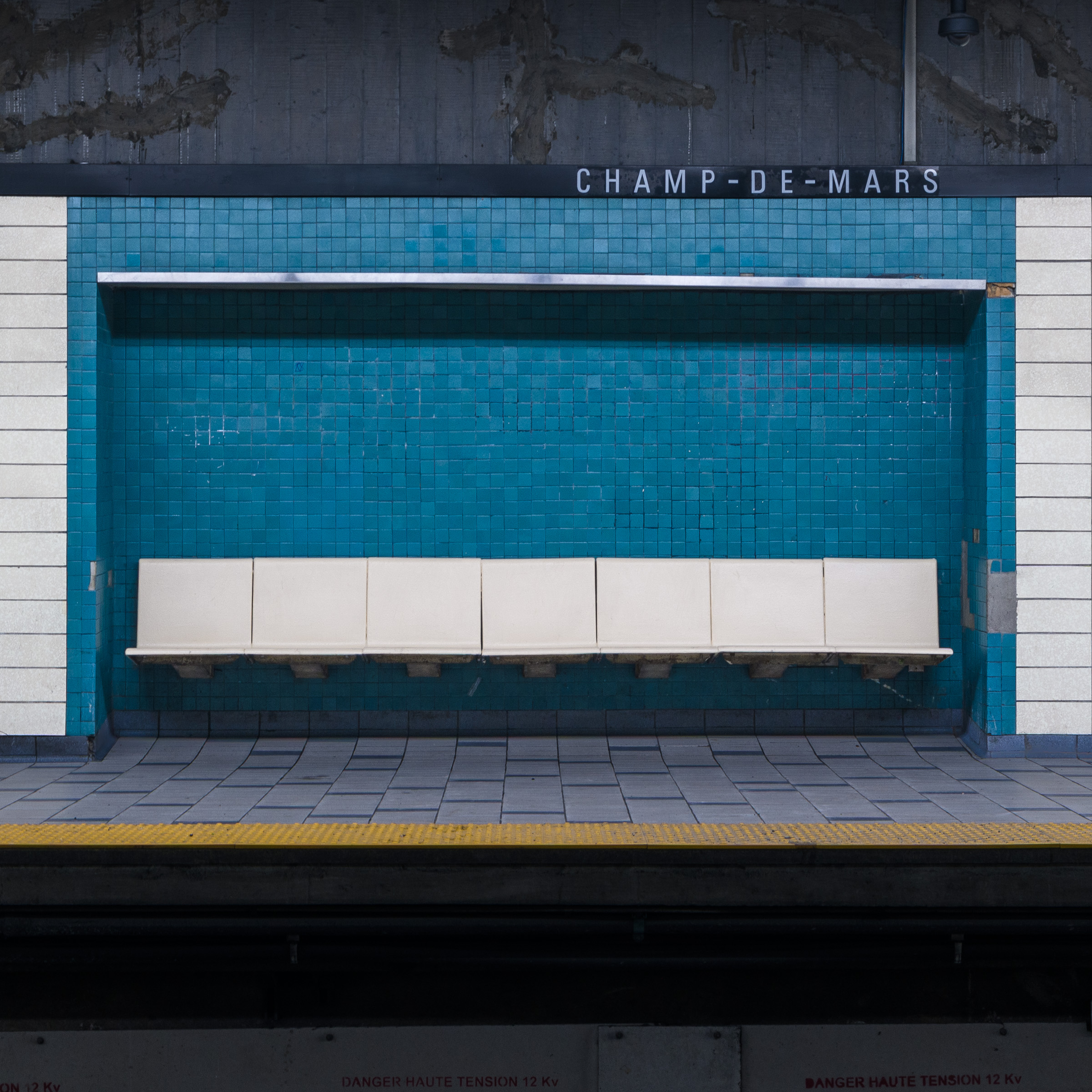 Colour photograph of white platform seating set against a blue tiled wall at Champ-de-Mars station in the Montréal Métro, viewed from the opposite platform.
