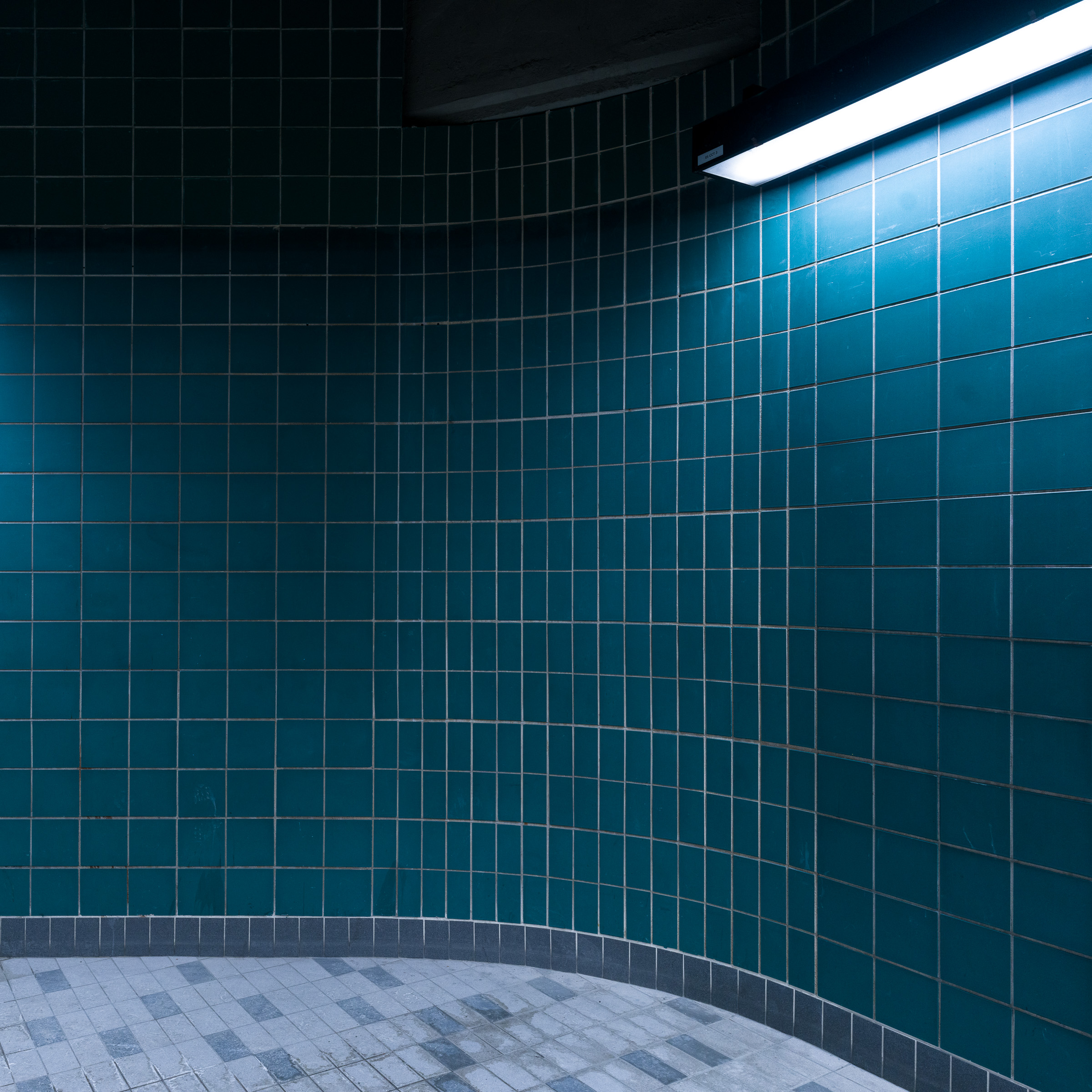 Colour photograph of blue tiled walls and a fluorescent light at the bottom of the stairs leading to the Champ-de-Mars platform in the Montréal Métro.