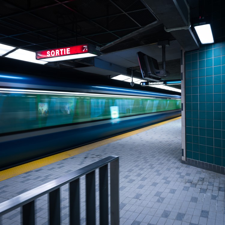 Long-exposure colour photograph of a train blurring past the Champ-de-Mars platform in the Montréal Métro, viewed from the platform entrance at the bottom of the stairs.