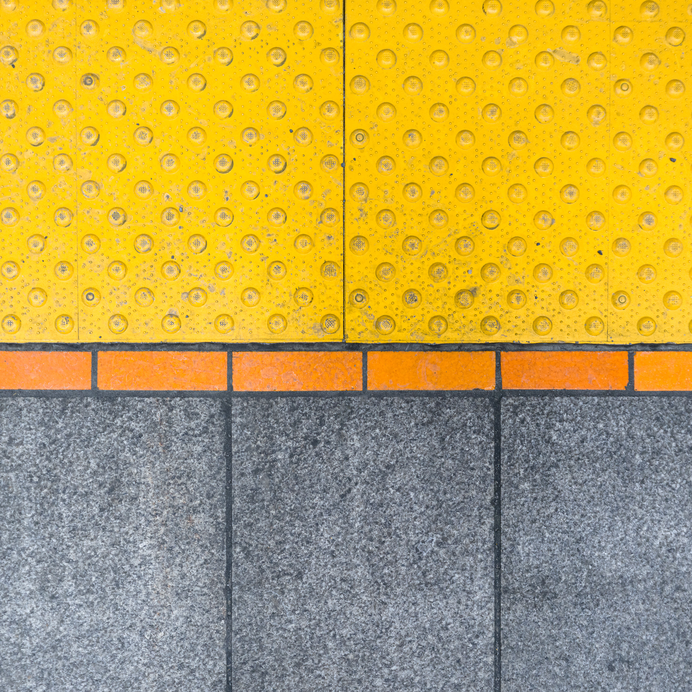 Colour photograph of mixed floor surfaces at Côte-Sainte-Catherine station in the Montréal Métro, showing yellow tactile paving, orange tiles, and grey stone.