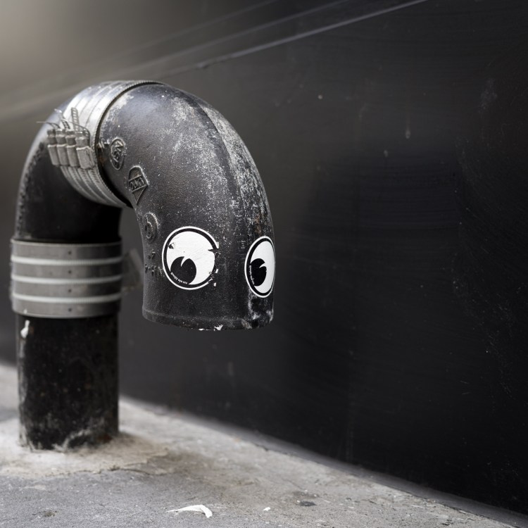 Black pipe with googly eyes attached, photographed against a dark wall.