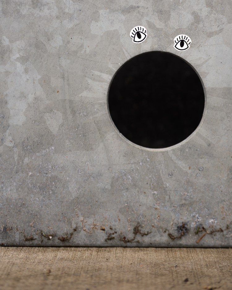 Small eye stickers above a large circular hole in a grey wall.
