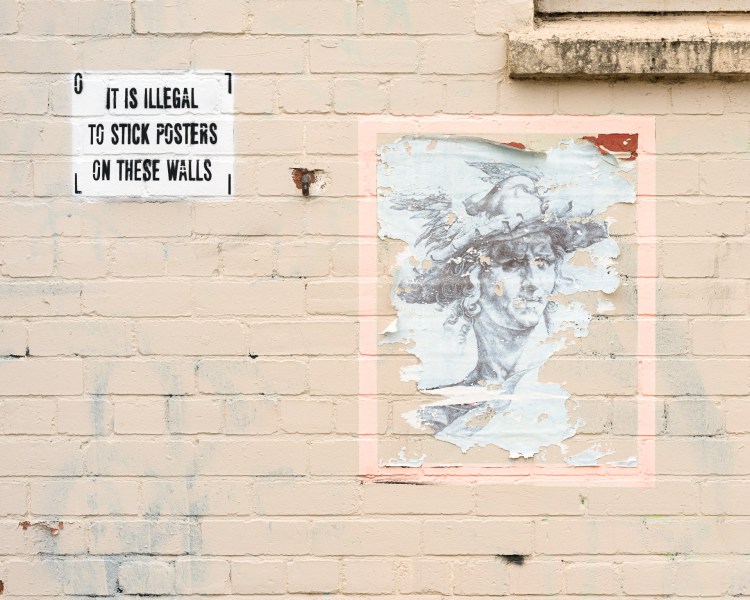 Peeling poster beside a notice reading “It is illegal to stick posters on these walls” in Bristol.