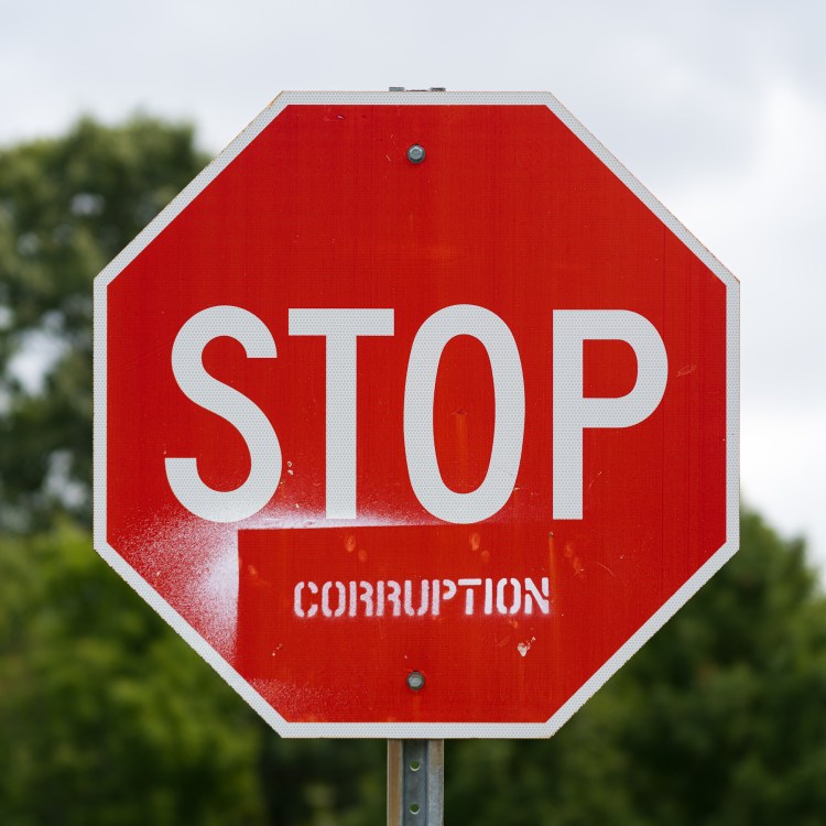 Red stop sign stencilled with the word “CORRUPTION” beneath STOP.