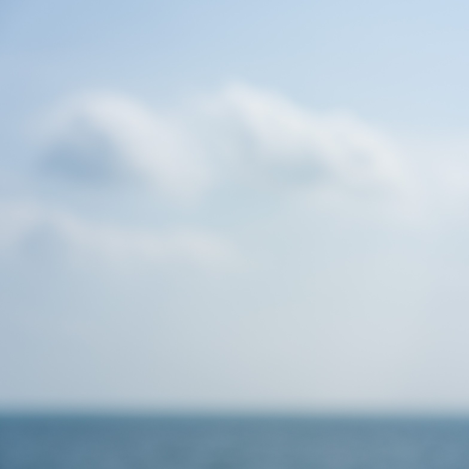 Deliberately out-of-focus view of Lake Ontario at Upper Gap, with a soft horizon beneath a pale blue, cloud-filled sky.