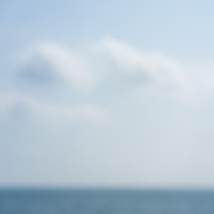 Deliberately out-of-focus view of Lake Ontario at Upper Gap, with a soft horizon beneath a pale blue, cloud-filled sky.