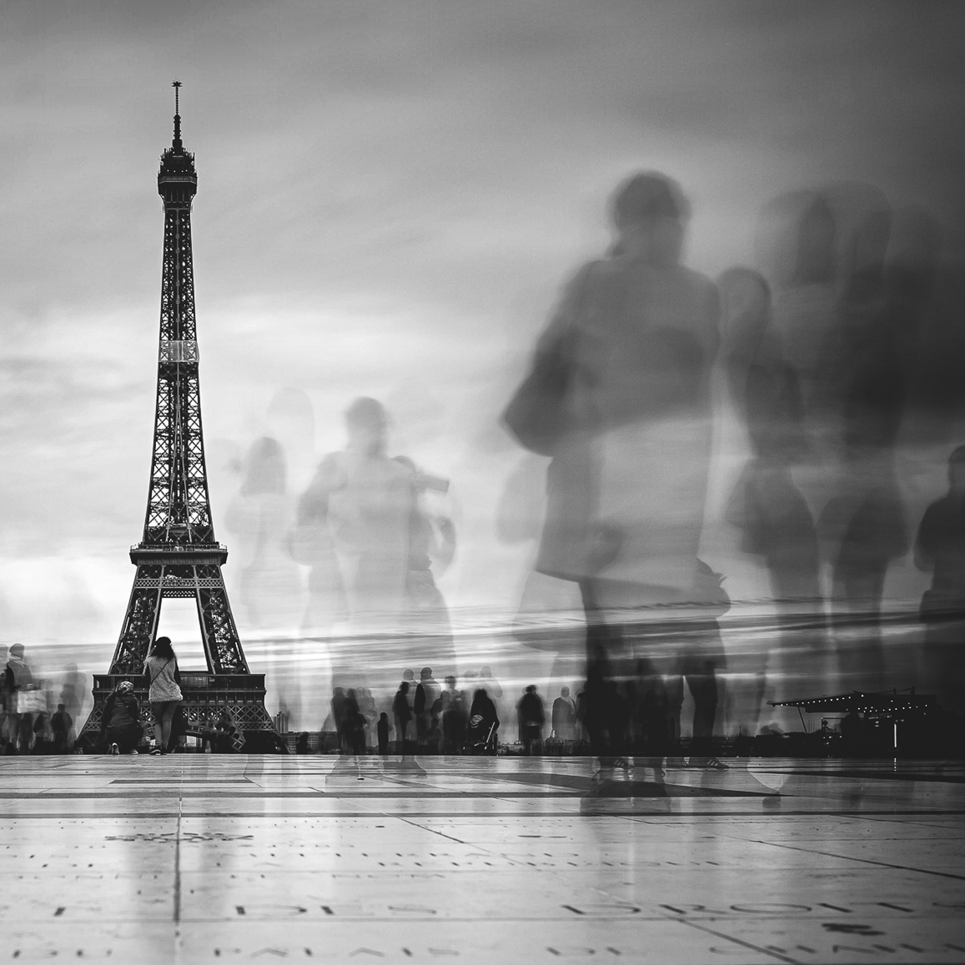 Black-and-white long exposure of crowds moving across the Trocadéro with the Eiffel Tower in the background.
