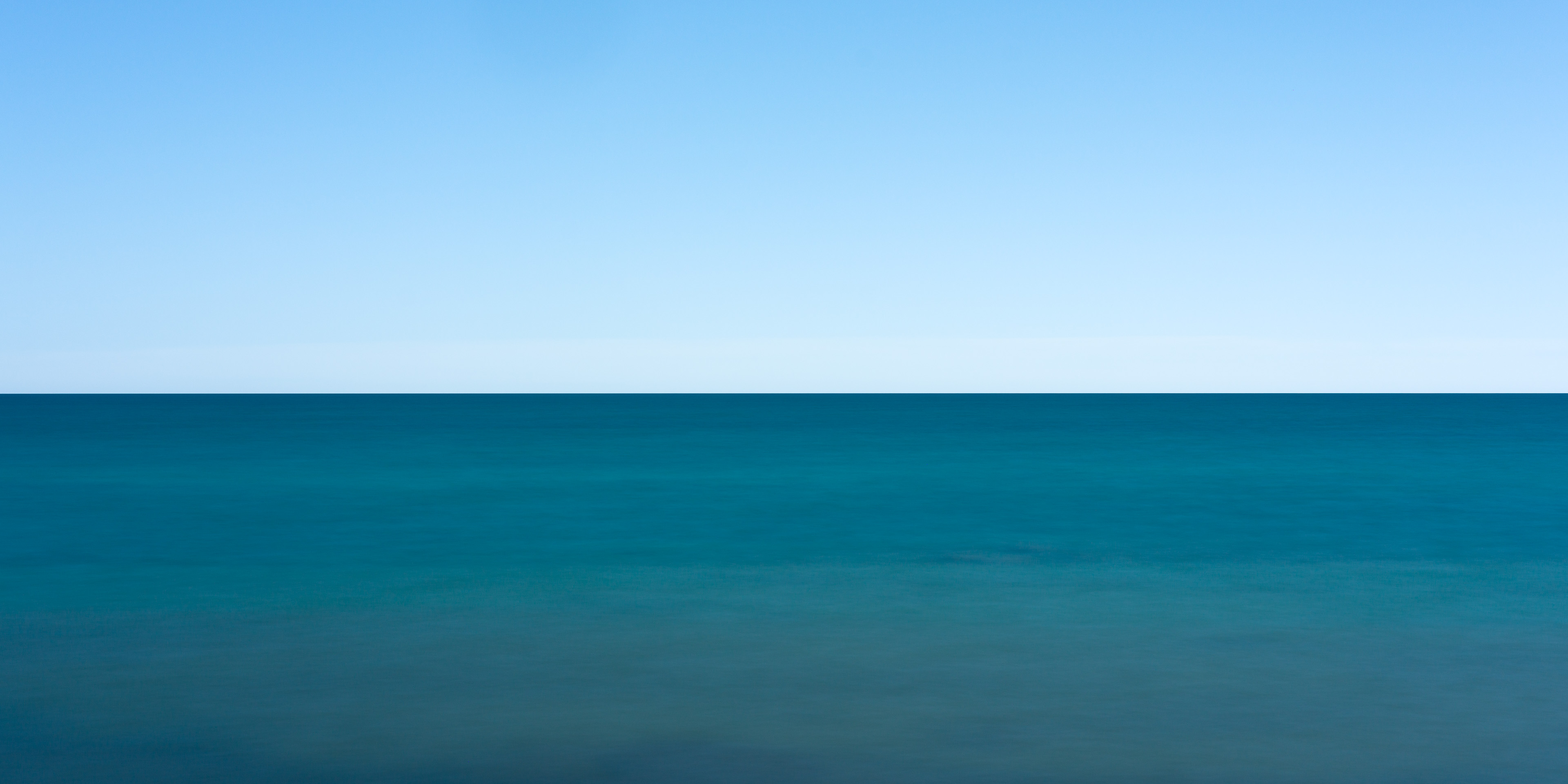 Minimalist long-exposure photograph of Lake Ontario, with a centred horizon dividing pale blue sky and deep blue-green water.