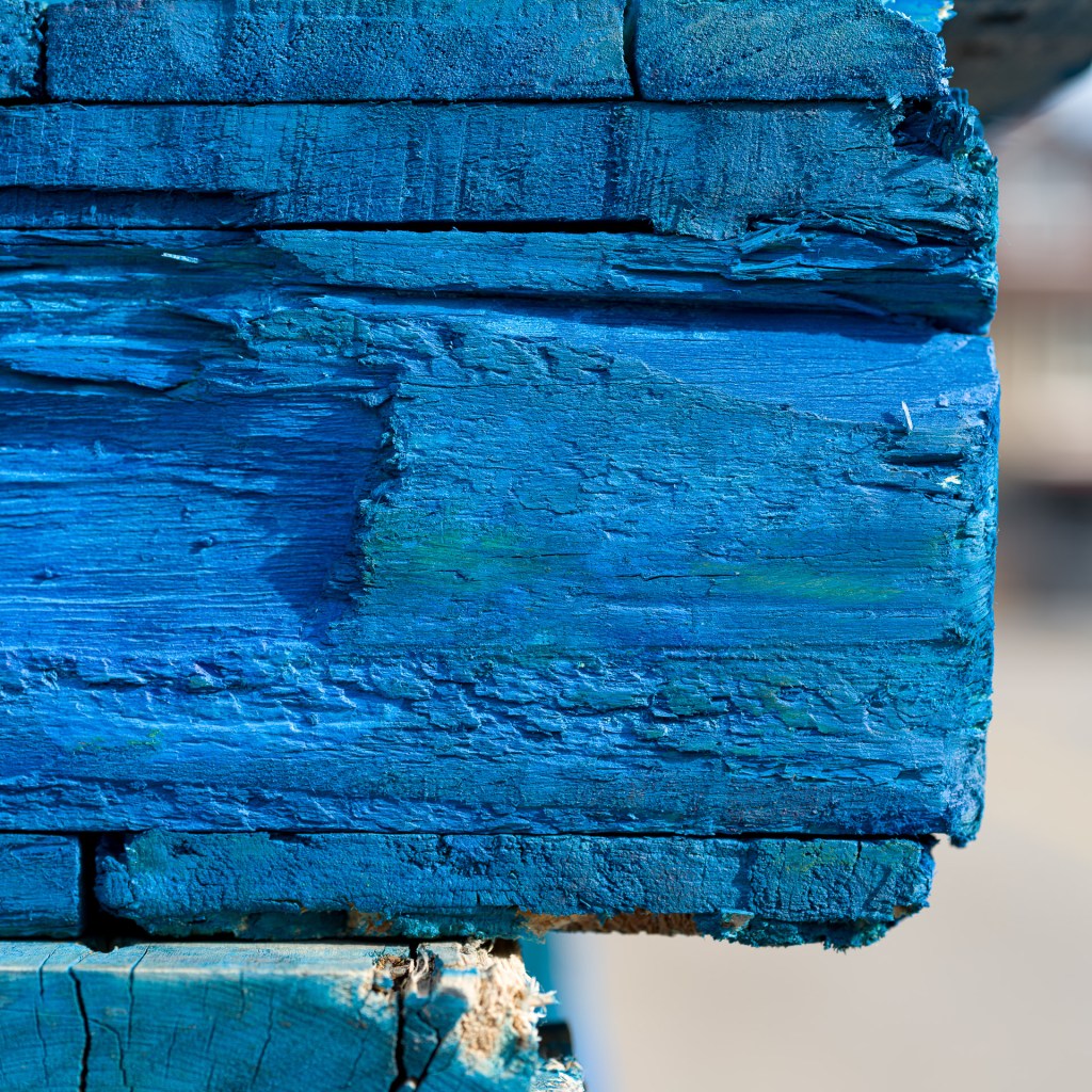 Close-up of a stack of weathered blue-painted wooden pallets with splintered edges and worn paint.