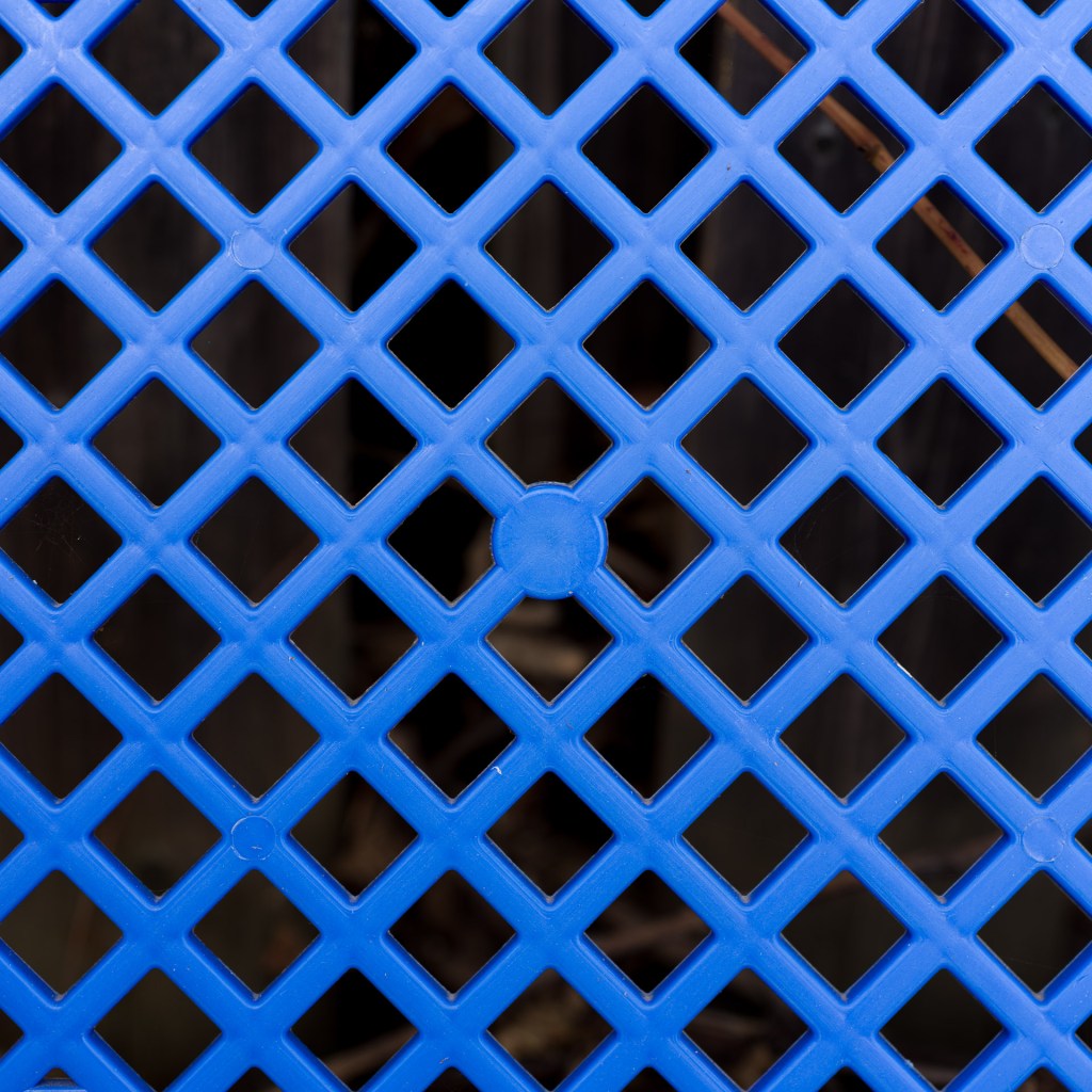 Close-up of a blue plastic bread crate with a repeating diamond lattice pattern.