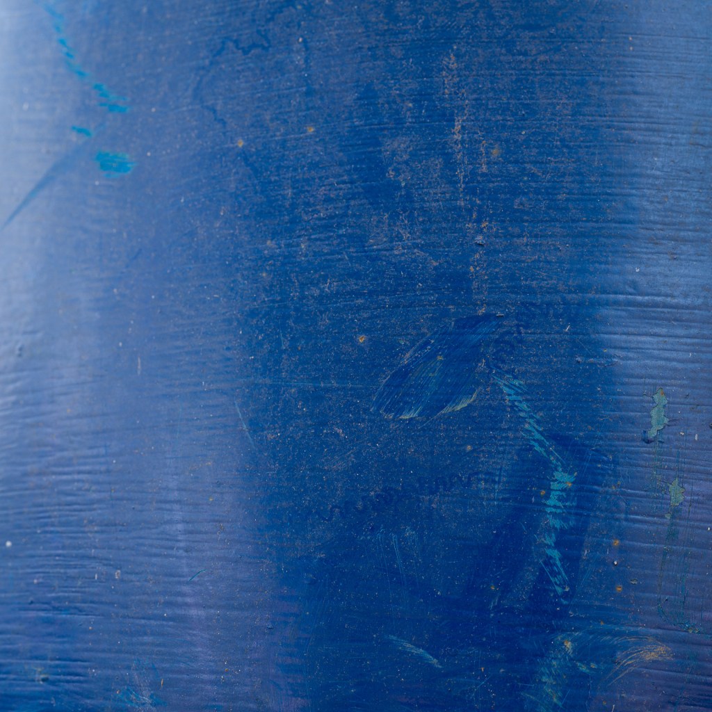 Close-up of a weathered blue waste-bin surface marked by scratches, scuffs and worn patches.