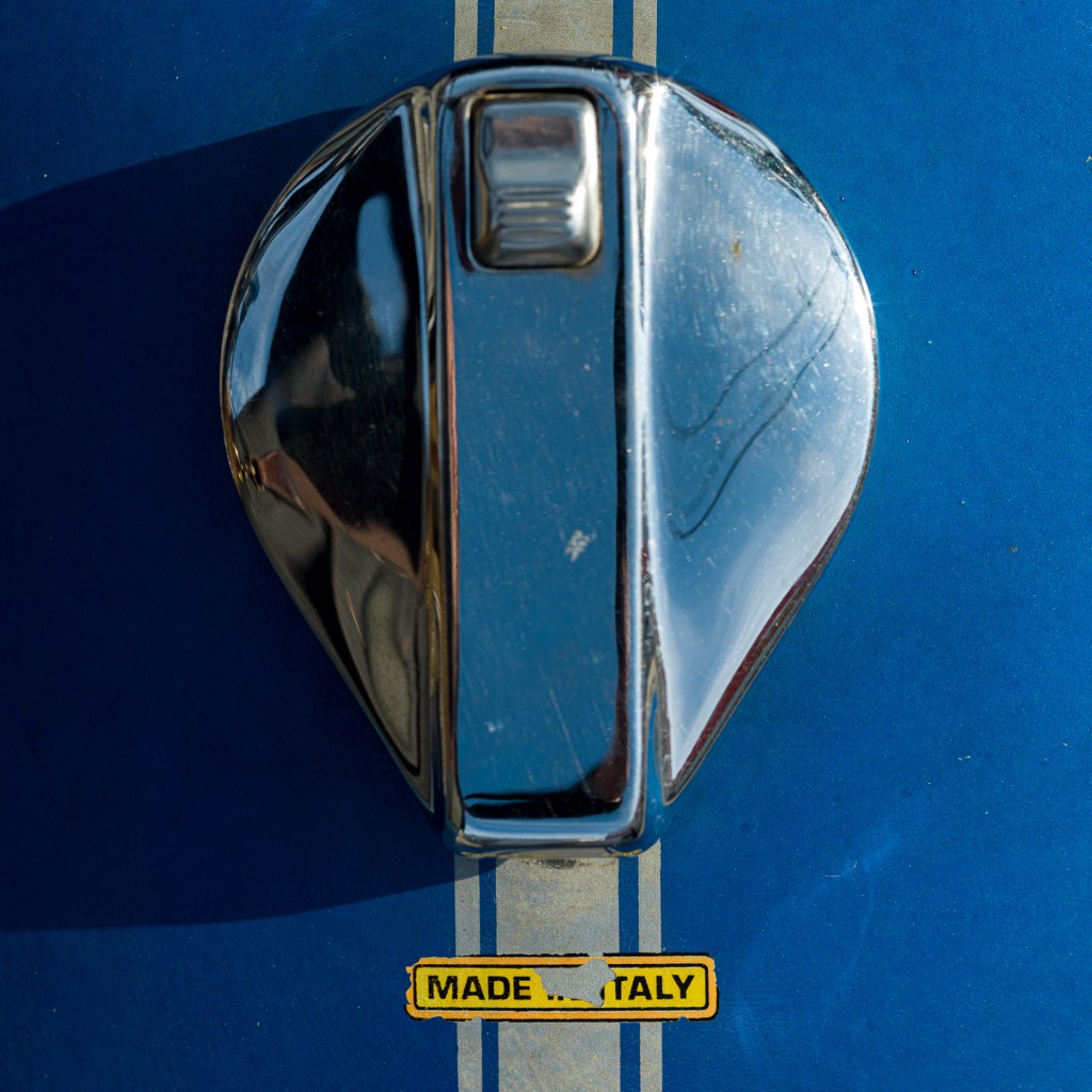 Chrome fuel cap on a blue 1978 Ducati 900 GTS motorcycle with cream racing stripes and a yellow “Made in Italy” label.