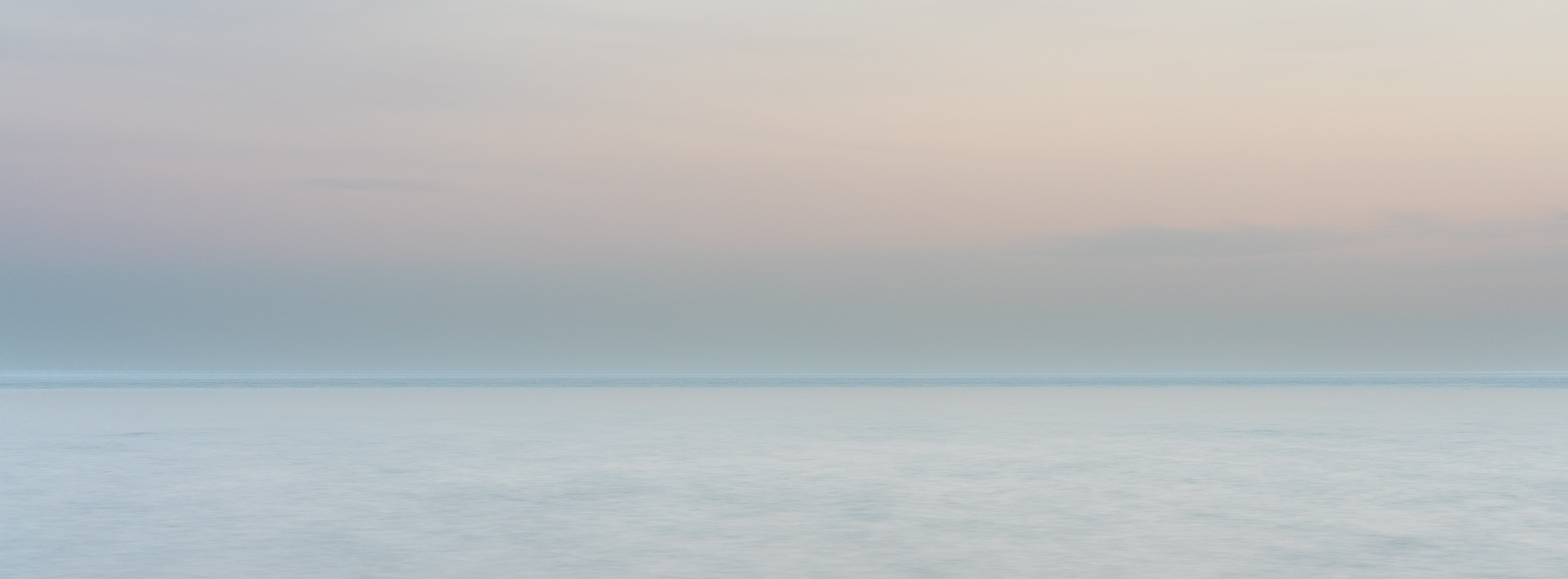 Long-exposure photograph of Lake Ontario at Upper Gap, with a pale blue horizon beneath soft pastel clouds.