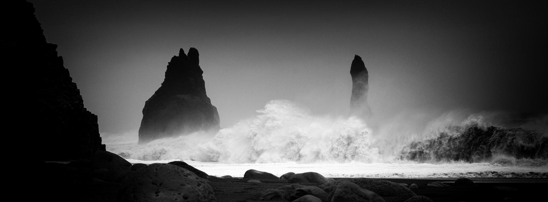 Black-and-white photograph of powerful waves breaking around the sea stacks at Reynisfjara black-sand beach in Iceland.