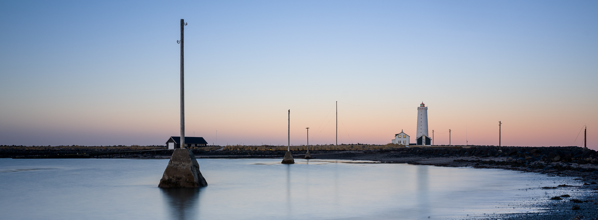Long-exposure sunrise view of Grótta Lighthouse near Reykjavík, Iceland, with calm water and pastel sky.