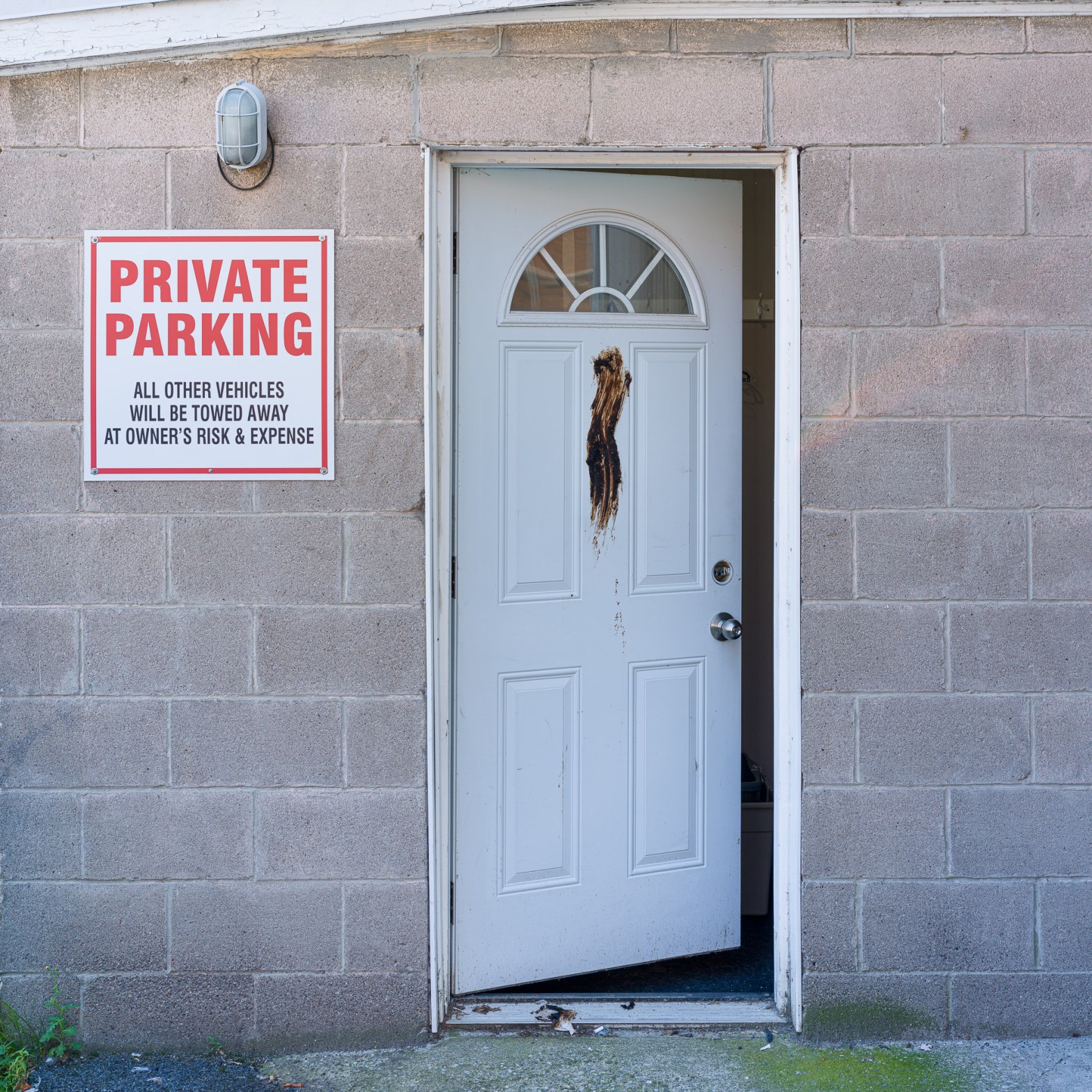 White commercial door left partly open beside a private parking sign, with a dark brown smear across the centre of the door.
