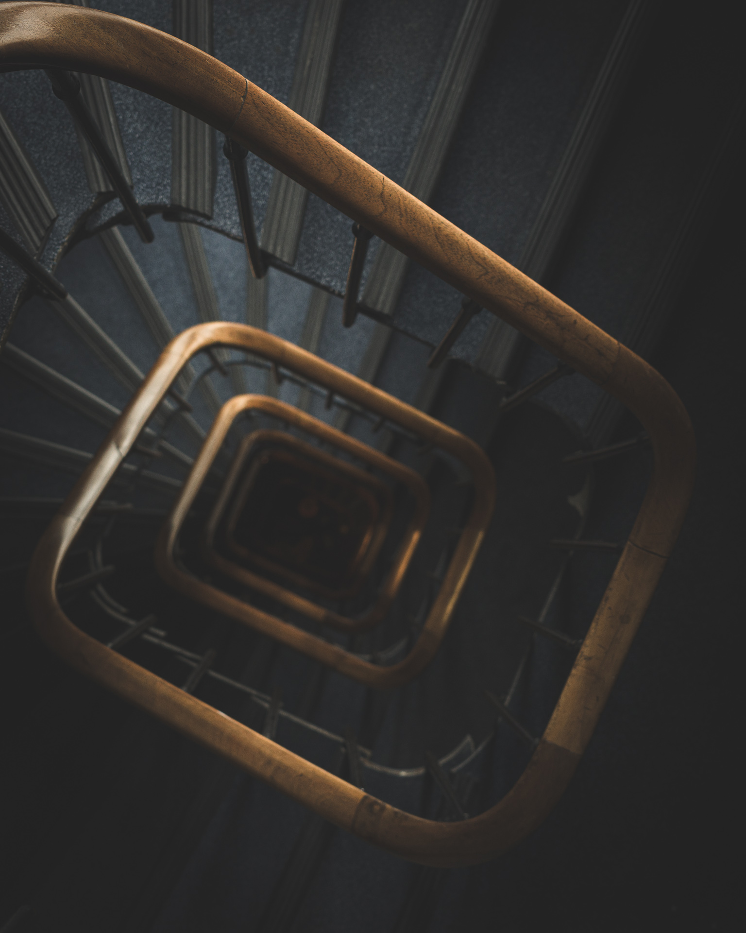 View looking down a Paris hotel staircase, with repeating wooden handrails forming a descending geometric spiral.